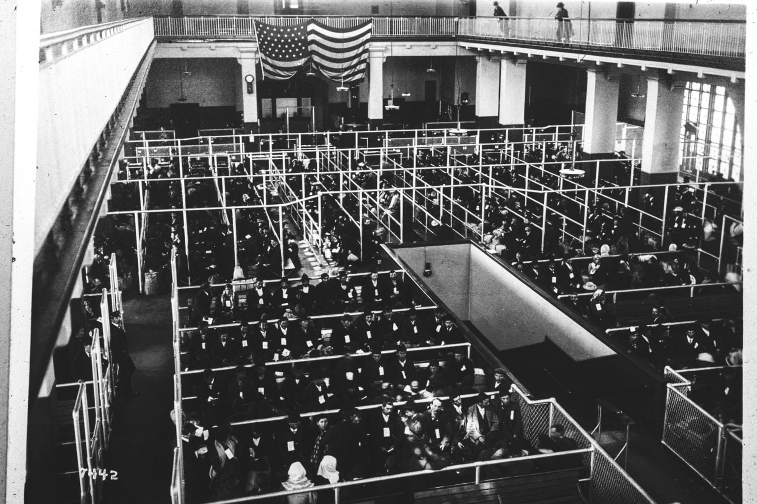 Immigrants in the railed pens of the Registry Room at Ellis Island in the early 1900s, waiting for inspection beneath the great vaulted hall.