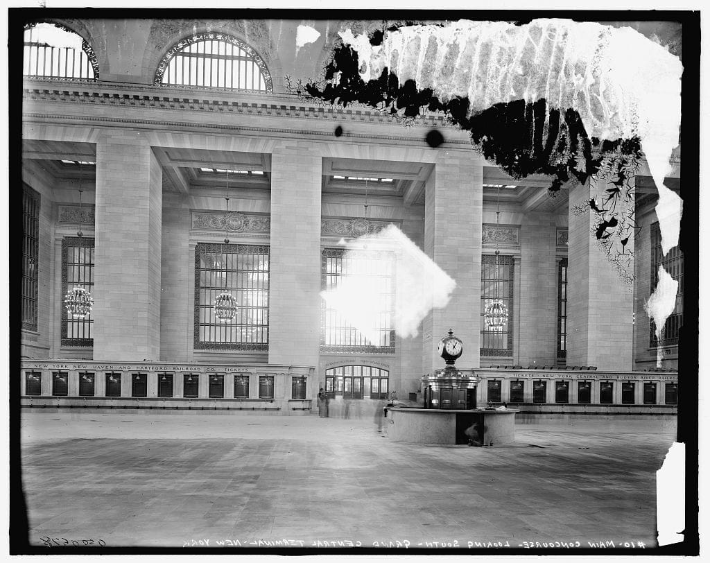 The Main Concourse of Grand Central Terminal looking south, sunlight streaming through the tall arched windows, in the early 1900s.