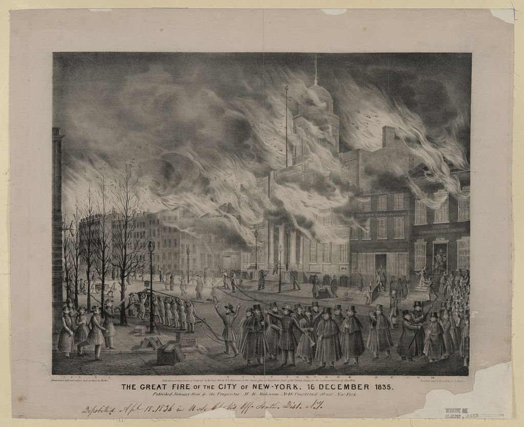 A black-and-white 1836 lithograph showing flames and billowing smoke engulfing multi-story buildings along a New York street, with firefighters, a hand-pumped engine and crowds of onlookers in top hats in the foreground.